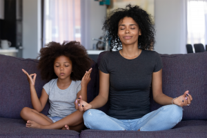 Mother and daughter meditating together on a gray couch
