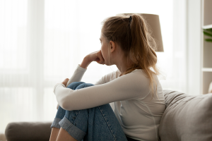 Girl with blonde ponytail sitting on a couch looking away from the camera with teen depression.