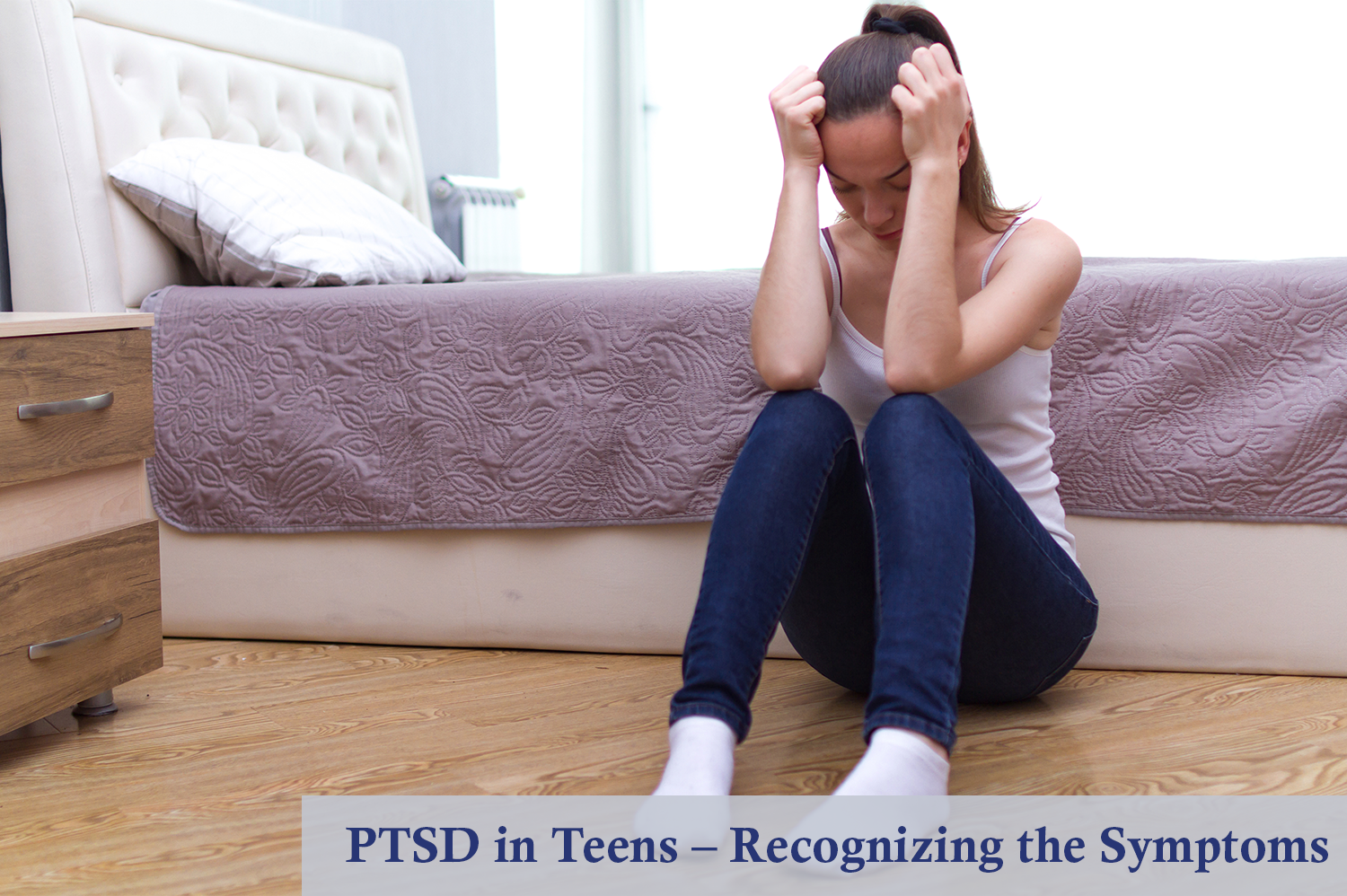 A teen girl sitting on the floor of their bedroom with her head in her hands - an example of PTSD in teens.