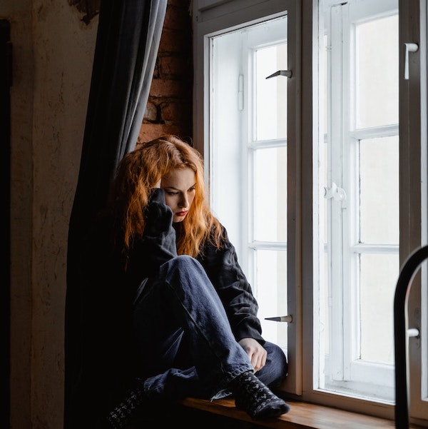 sad woman sitting on a window sill